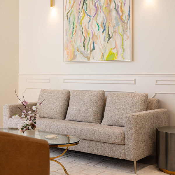lakemans Jewelry one-on-one consultation with designers, featuring cozy modern interior with gray sofa, gold glass coffee table, floral arrangement, and abstract artwork.