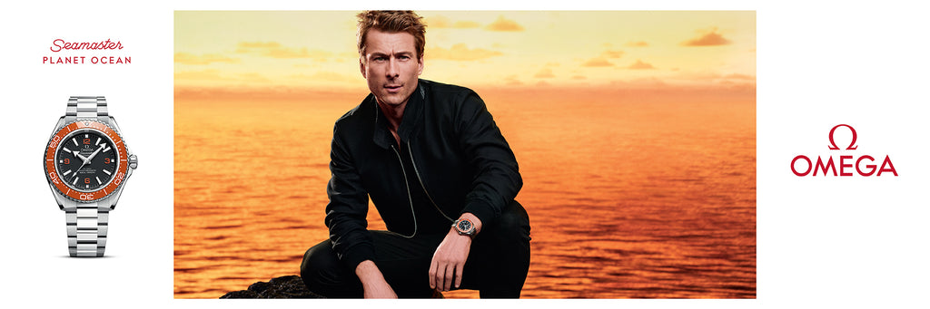 Omega Seamaster Planet Ocean luxury watch with orange bezel, showcased at sunset ocean backdrop.